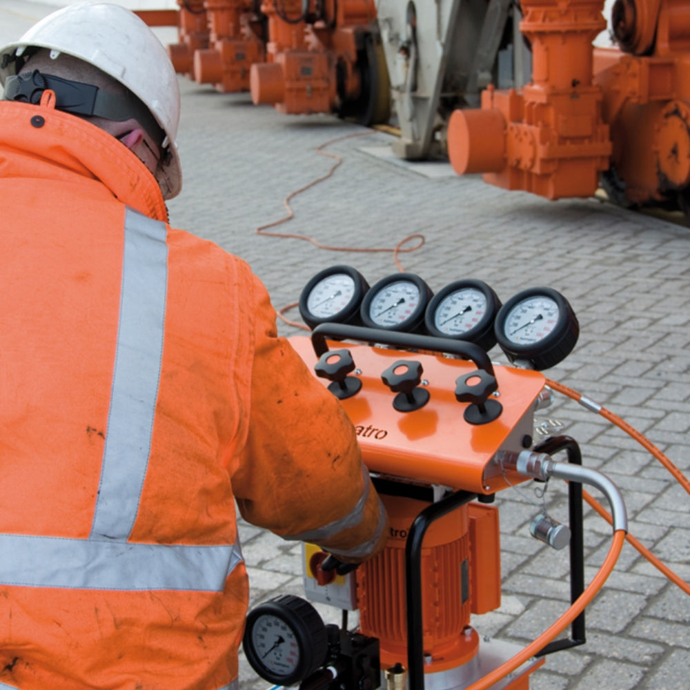 Person i orange dragt bruger Holmatro manifold med fem manometre og knapper.