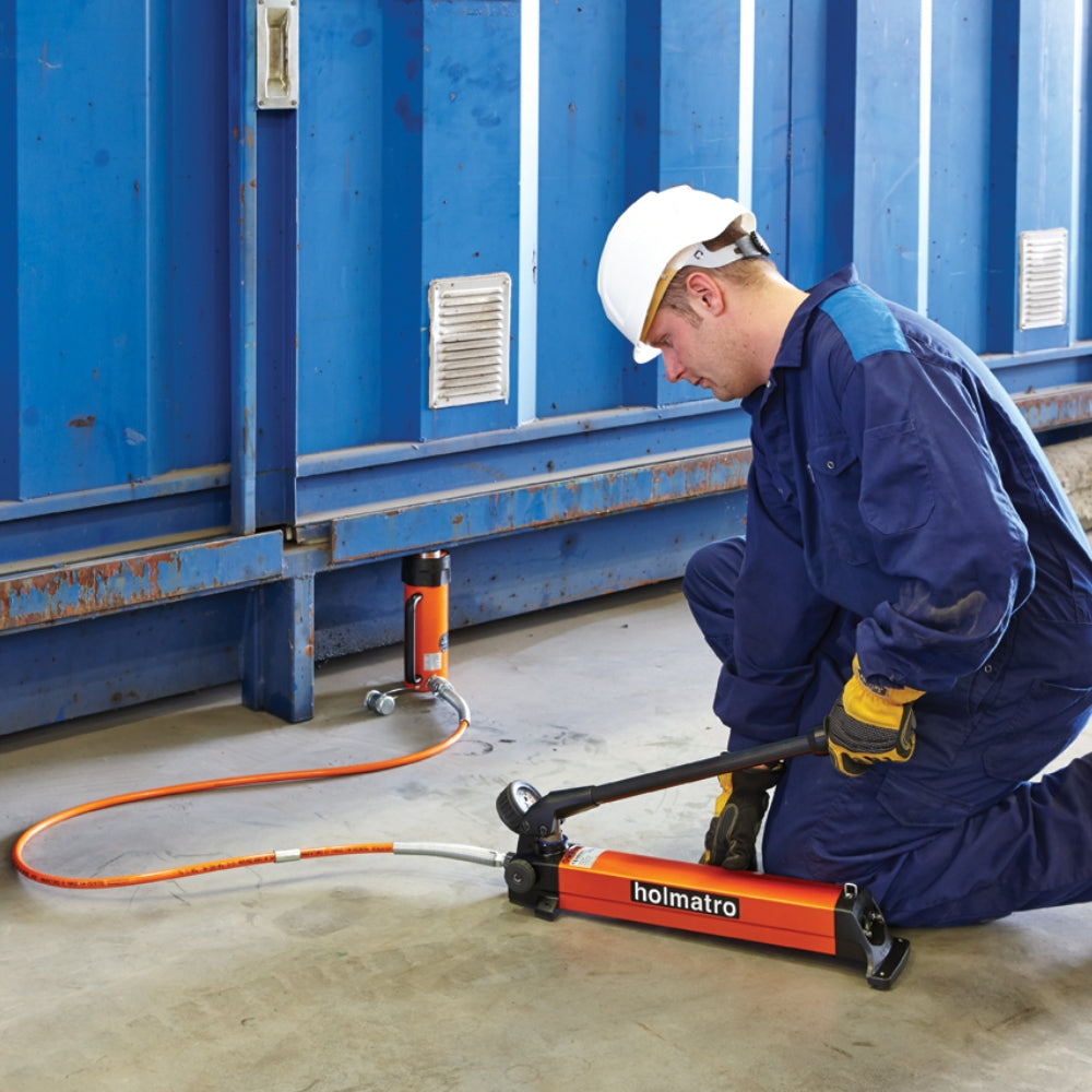 Person i arbejdstøj bruger Holmatro Håndpumpe - PA 18 H 2 ved blå container.