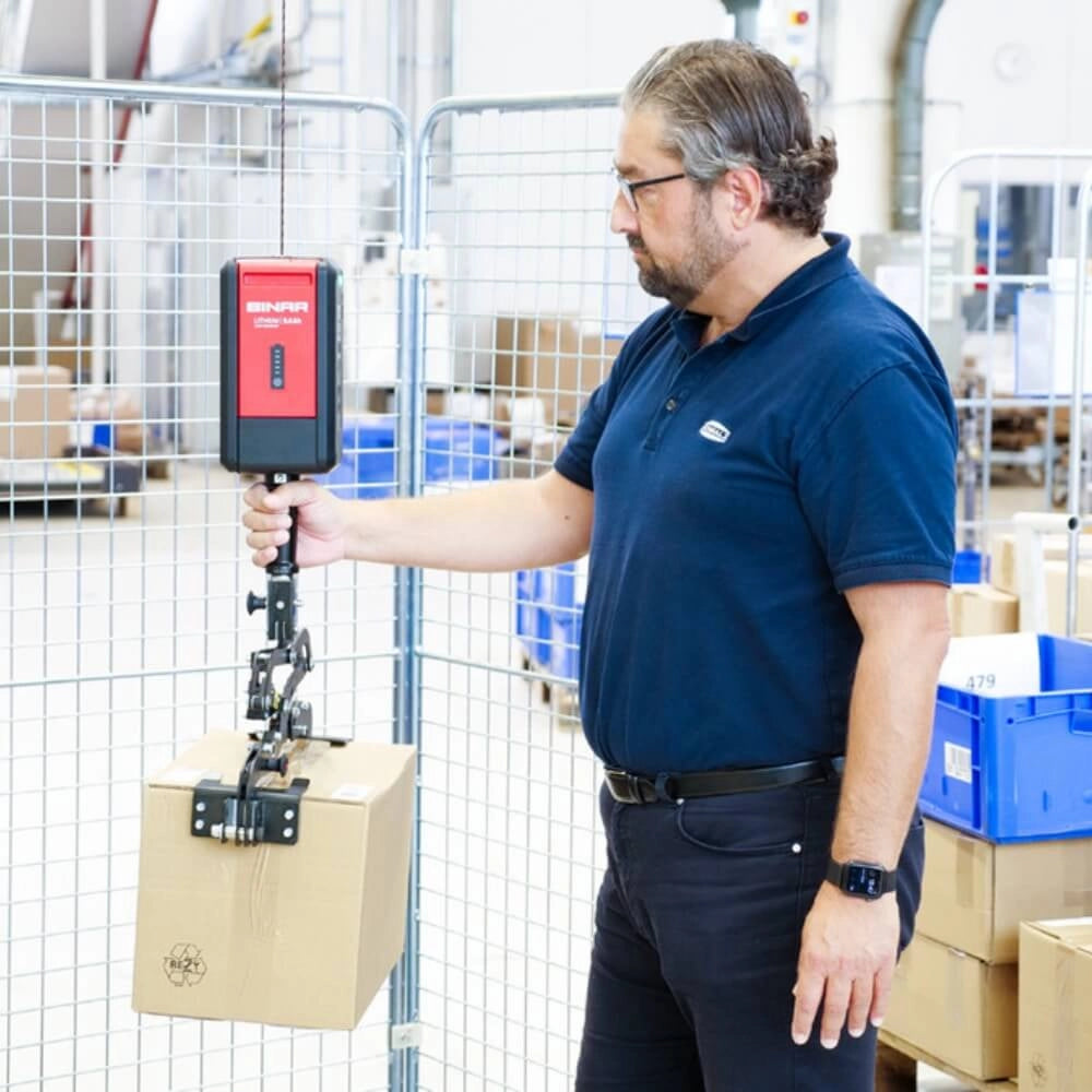 En person bruger Binar El balance talje NEO30 1400EL til at løfte en kasse i et lager.