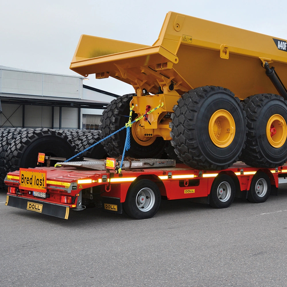 Stor gul maskine på rød trailer, sikret med GrabiQ Kædestrammer Type GT-10 og kæder.