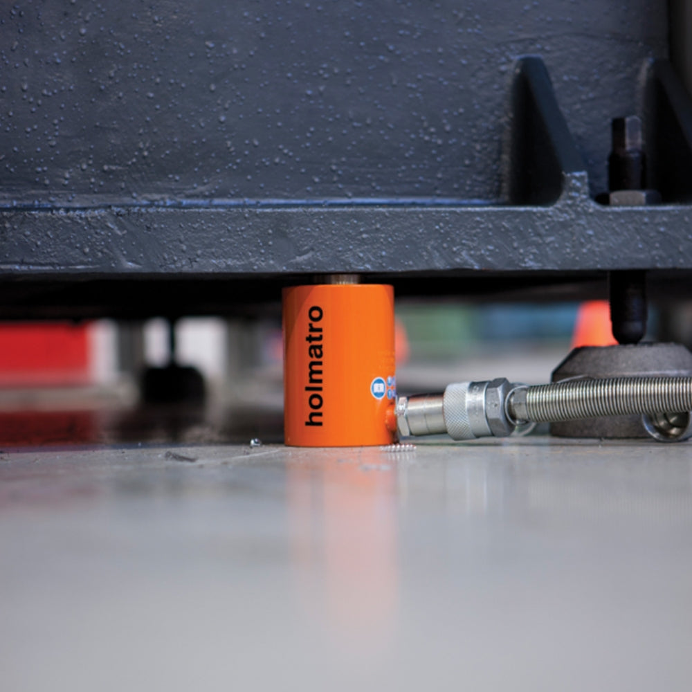 Orange Holmatro donkraft løfter tung genstand. Sort håndtag og slange ses tydeligt.