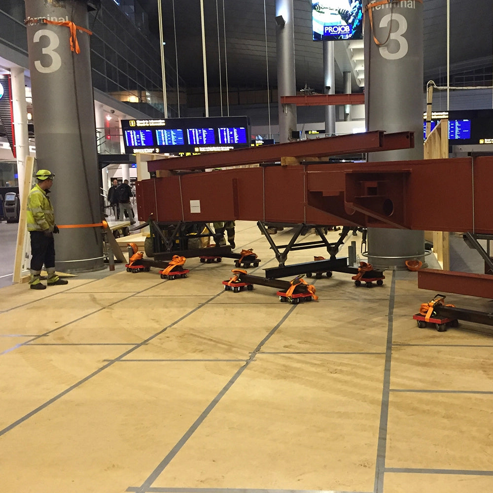 Stor struktur flyttes i terminal ved hjælp af flere røde transporthjul med orange stropper.