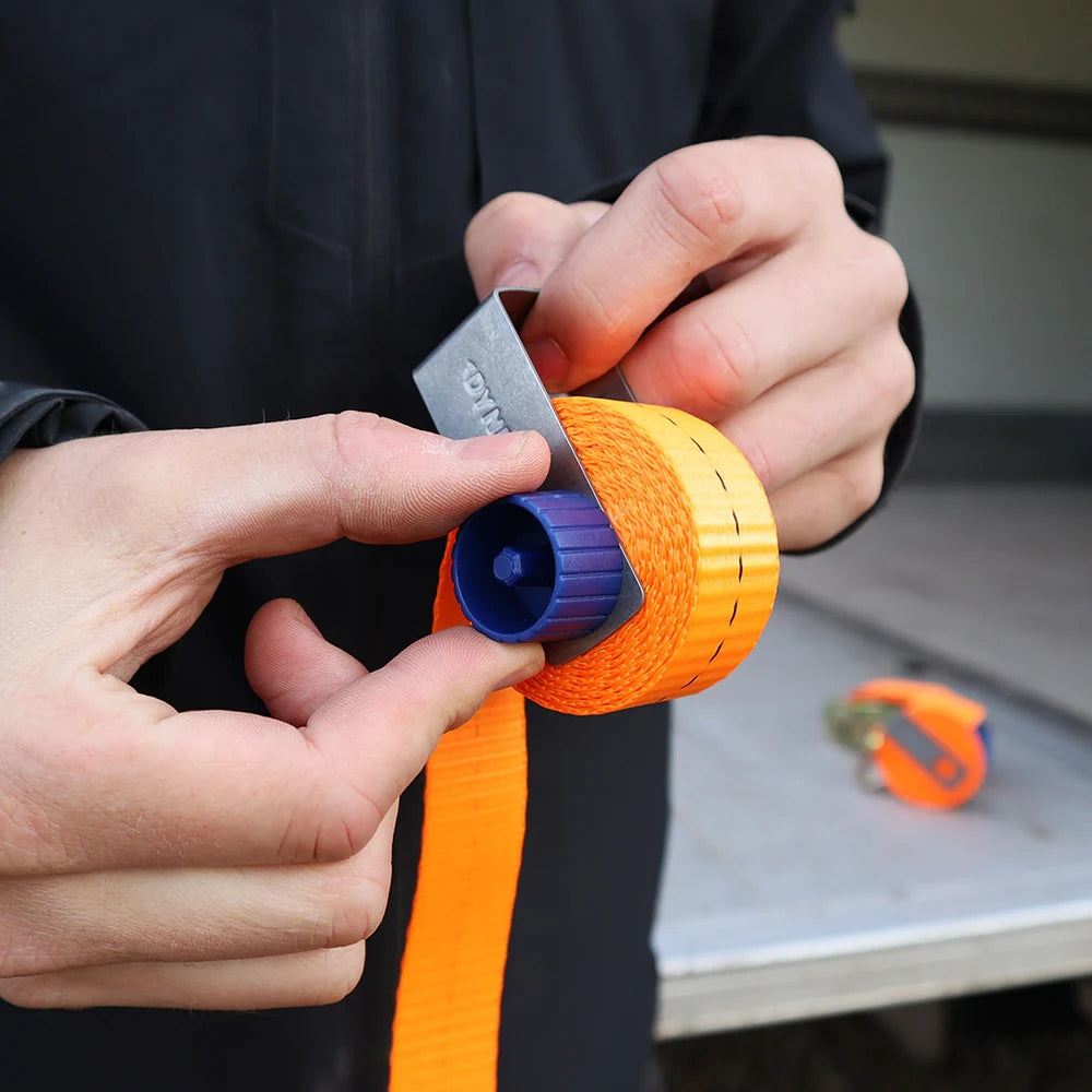 Hænder bruger Dynello surringsbånd clip med blå opruller og orange bånd på grå baggrund.