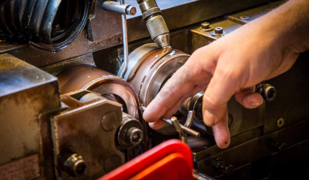 Hånd justerer metal på drejebænk, viser præcisionsarbejde med fokus på detaljer og håndværk.