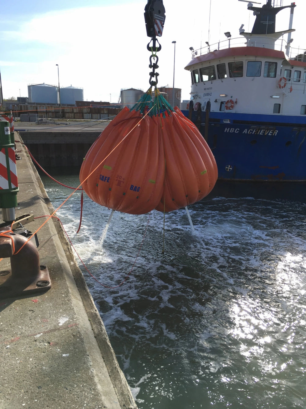 Orange vandpose "SAFE T BAG 2T" hænger over vand ved kaj, maritime omgivelser, robust design.