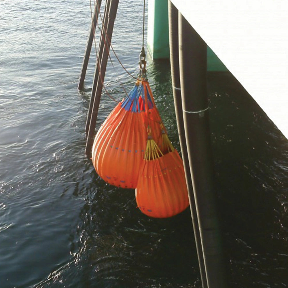 To orange vandposer hænger over vand i maritimt miljø, brugt til vægtbelastning.