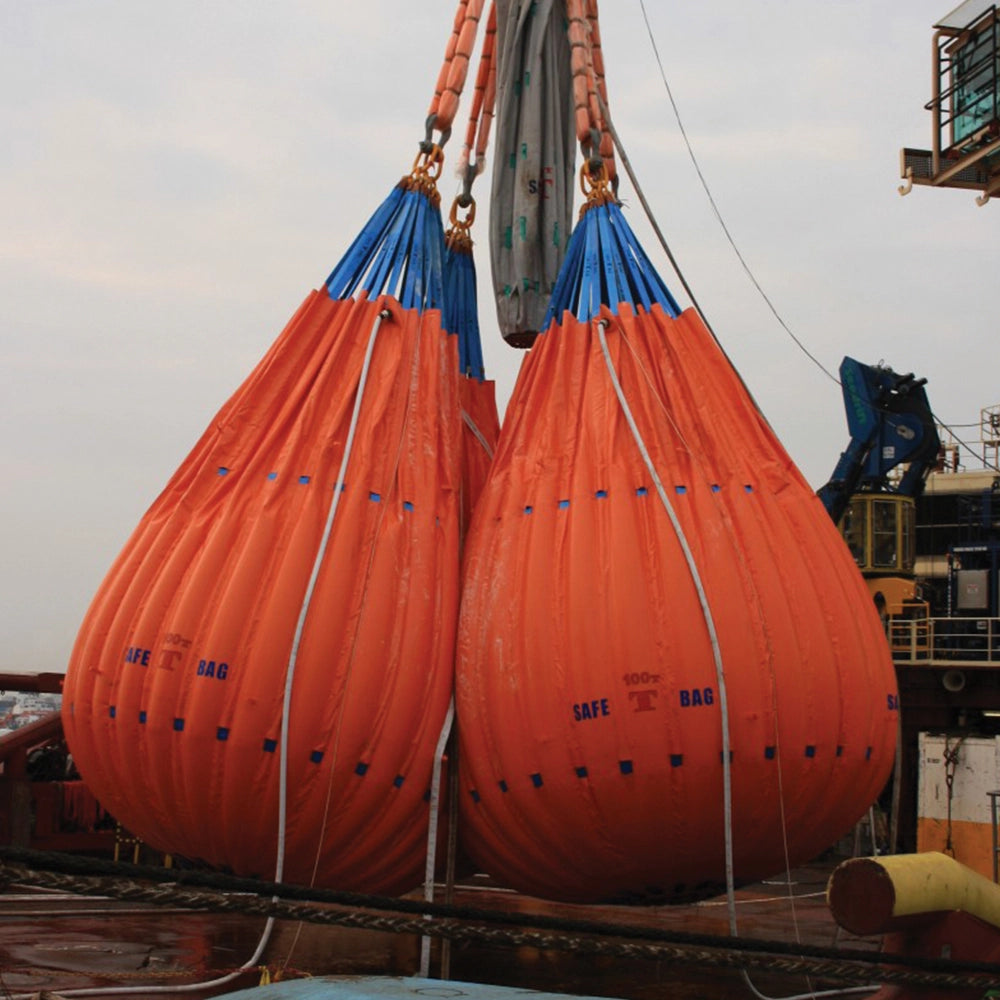 To orange vandposer med "SAFE T BAG" og "2T" hænger i maritime omgivelser med blå stropper.